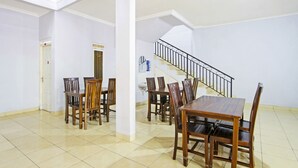 A spacious dining area with a large wooden table and chairs, a tiled floor, and a staircase with a black railing. - Hotel O Homestay Al Maidah (Depok)