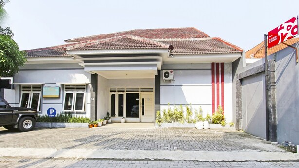 A building with a tiled roof, a covered entrance, and a parking sign. - Hotel O Homestay Al Maidah (Depok)
