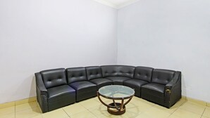A corner room with a black leather sectional sofa and a glass coffee table. - Hotel O Homestay Al Maidah (Depok)