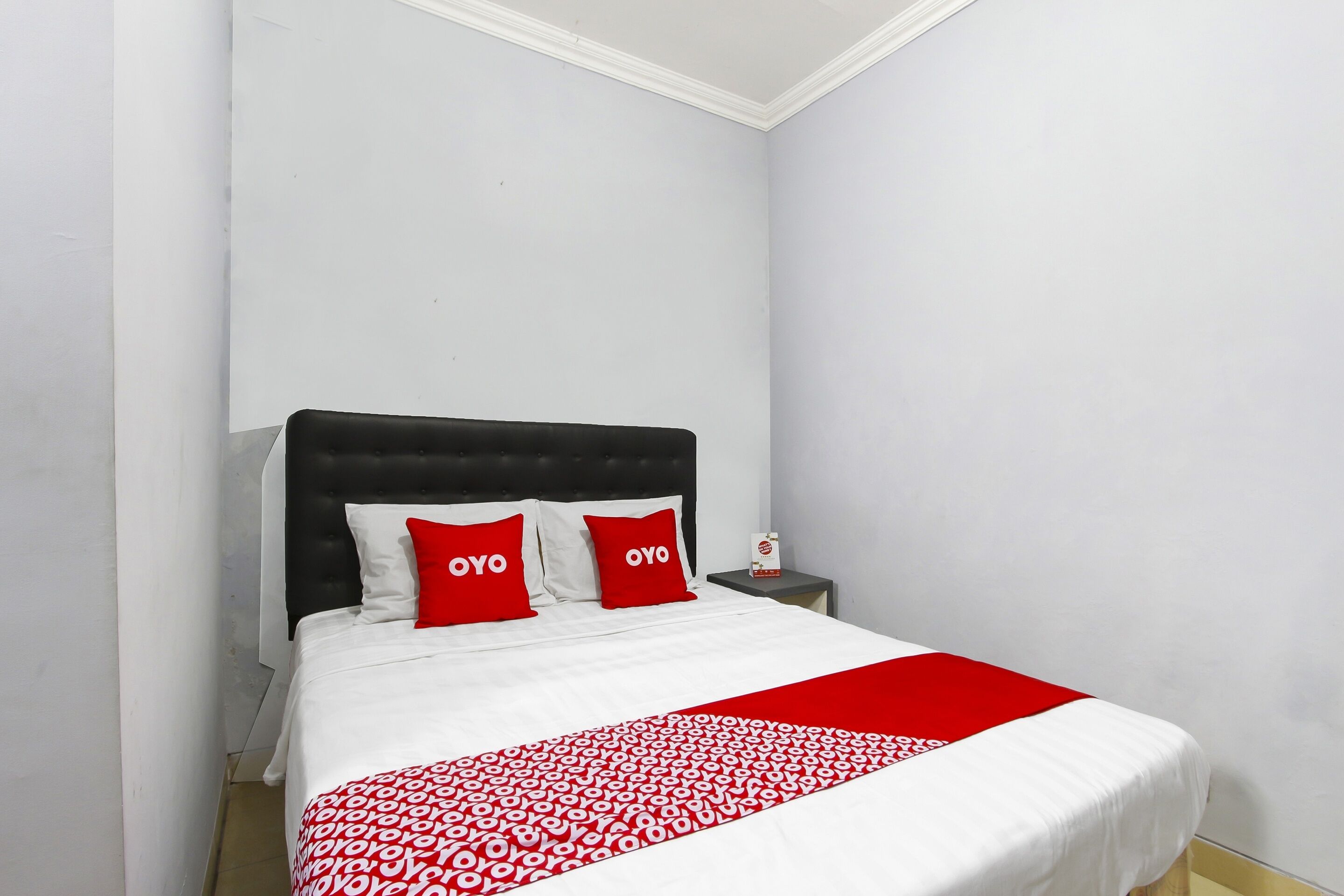 A bed with a black headboard, white bedding, and two red pillows with the word "OYO" on them.
