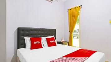 Quarto de hotel com uma cama, cabeceira, mesa de cabeceira, janela com cortinas amarelas e um ar condicionado na parede.