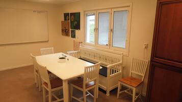 A conference room with a white table, white chairs, a whiteboard, and a window with blinds.