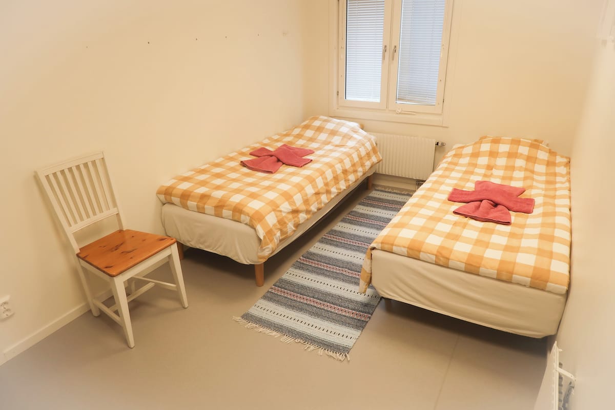 Une petite chambre propre, avec deux lits simples, une chaise en bois et un tapis à rayures.