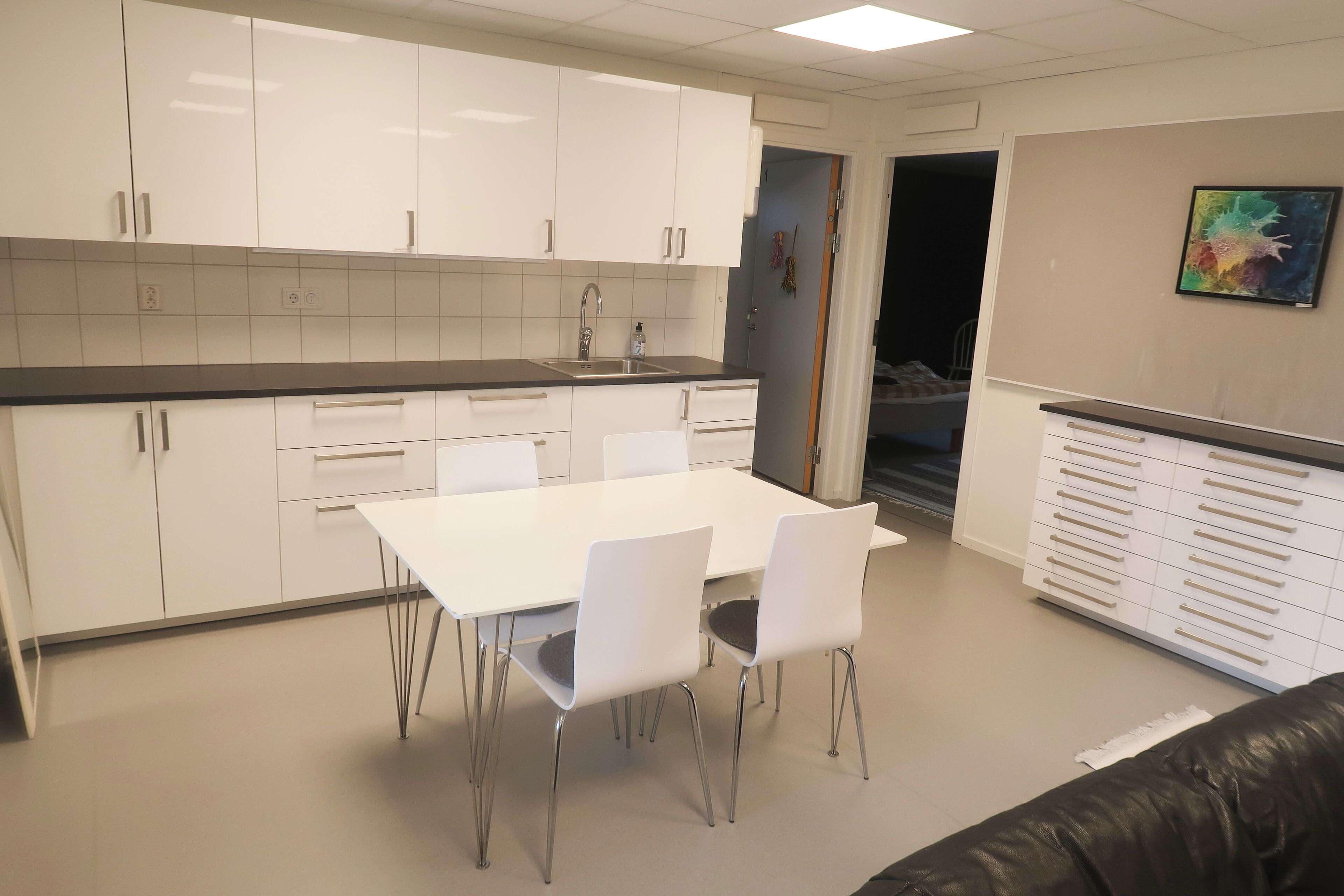 Una cocina moderna con armarios blancos, encimera negra y un comedor con sillas blancas.