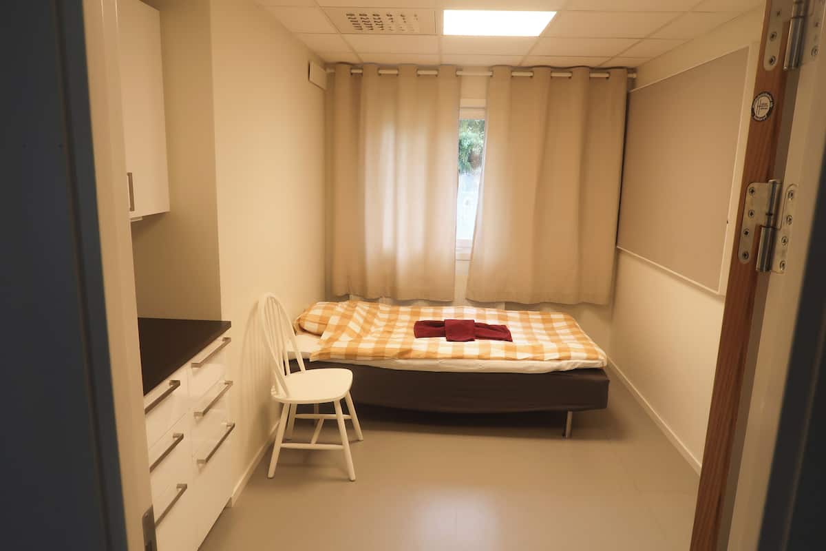 Une petite chambre à coucher, de taille modeste, comprenant un lit simple, une chaise et une commode.