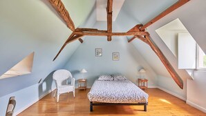 A bedroom with a sloped ceiling, wooden beams, a bed, a chair, and two bedside tables. - Maison de Caractere à la Campagne (Saint-Geyrac)