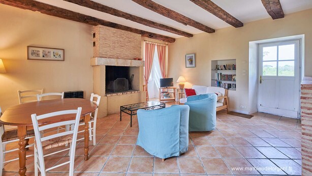 A cozy living room with a fireplace, a dining table with chairs, a sofa, and a bookshelf. - Maison de Caractere à la Campagne (Saint-Geyrac)