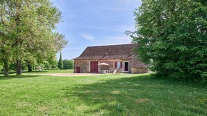 A rustic stone building with a red door, surrounded by a grassy lawn and trees. - Maison de Caractere à la Campagne (Saint-Geyrac)