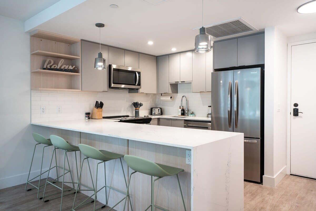A modern kitchen with a central island, bar stools, a microwave, a refrigerator, and a built-in oven.