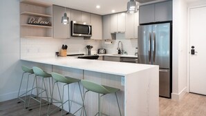 A modern kitchen with a central island, bar stools, a microwave, a refrigerator, and a built-in oven.