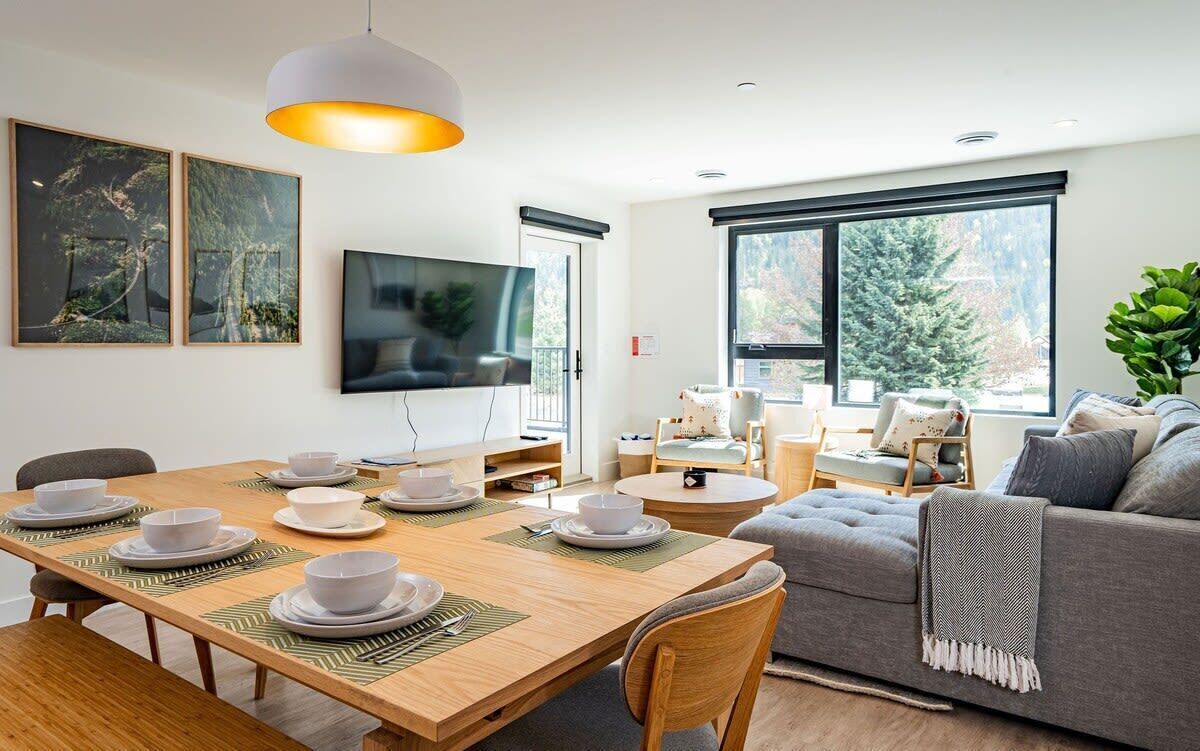 A modern living room with a dining area, large windows, and a grey sofa.