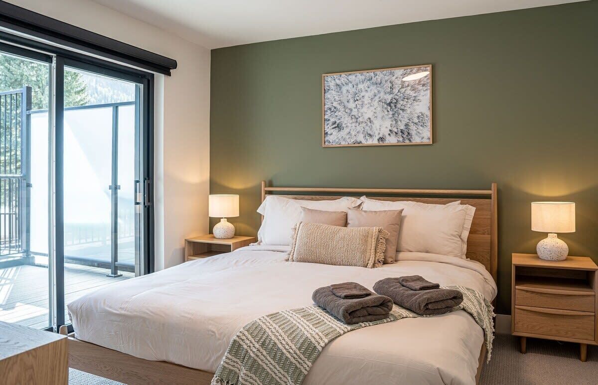 A bedroom with a bed, two bedside tables, a nightstand, a window with a view, and a wall-mounted artwork.