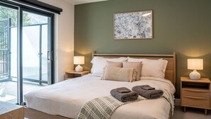 A bedroom with a bed, two bedside tables, a nightstand, a window with a view, and a wall-mounted artwork.