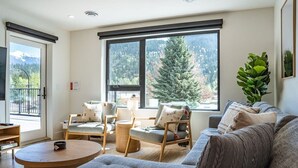 A modern living room with a sofa, two armchairs, a coffee table, and large windows with a mountain view.