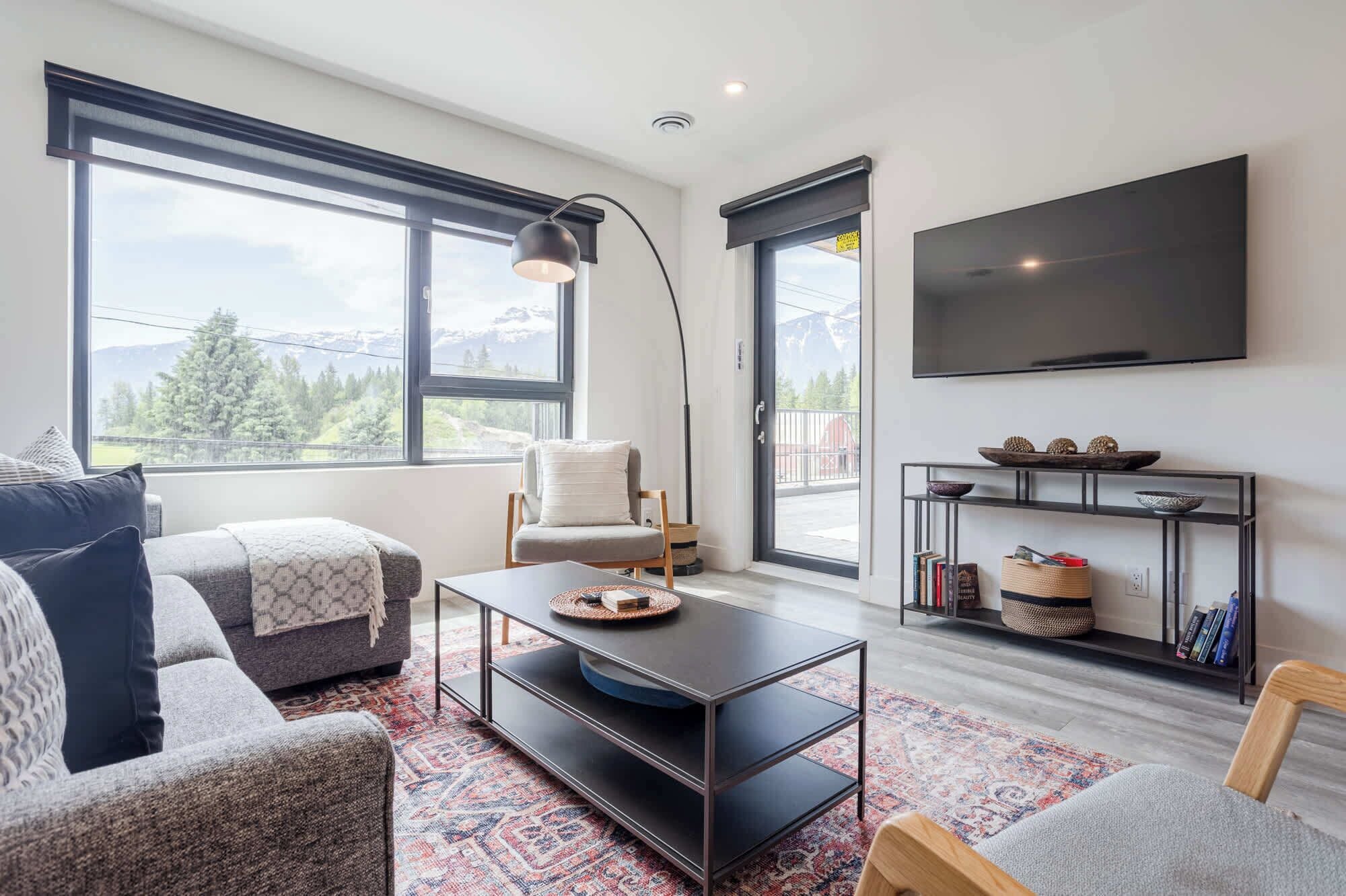 Una sala de estar moderna con sofá, sillón, mesa de centro y televisor montado en la pared.
