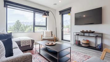 Una sala de estar moderna con sofá, sillón, mesa de centro y televisor montado en la pared.