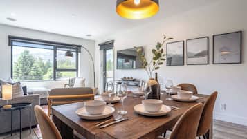 Un comedor con una mesa de madera dispuesta para cuatro personas, un sofá, un televisor y cuadros en la pared.