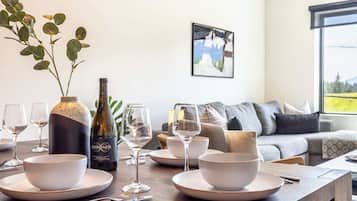 Comedor con una mesa dispuesta para cuatro personas, una botella de vino y un florero con hojas verdes.