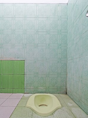 A small, tiled bathroom with a single toilet, green and white patterned walls, and a green partition. - SPOT ON 92373 Kristin Homestay 2 (Pati)