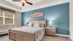 A bedroom with a large bed, two bedside tables, a ceiling fan, and a window with blinds. - 9817 Cristalino Way #102 (Fort Myers)