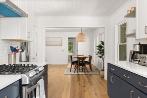 A kitchen with white cabinets, a stove, a dining table with chairs, and a hanging light fixture.
