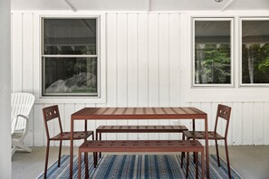 Una habitación con una pared de madera blanca, un ventanal grande, una mesa con sillas y una alfombra estampada.