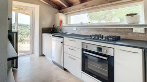 A modern kitchen with wooden beams, a built-in oven, and a window overlooking greenery. - Location Saisonnière Atypique à Porticcio (PORTICCIO)