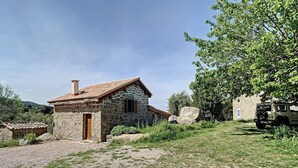 A stone house with a tiled roof, a gravel driveway, and a parked vehicle. - Location Saisonnière Atypique à Porticcio (PORTICCIO)