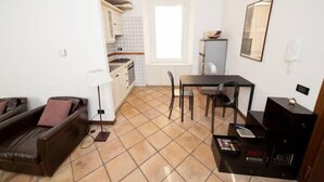 A compact living space with a sofa, a dining table with chairs, a small kitchen area, and a large window providing natural light. - 1 bedroom apartment in rome (Roma)