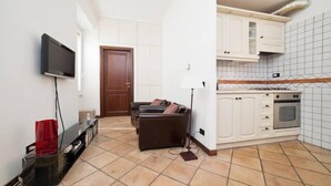 A compact living space with a kitchenette, a flat-screen TV mounted on the wall, a sofa, and a floor lamp. - 1 bedroom apartment in rome (Roma)