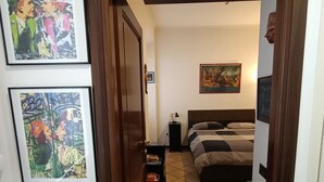 A hallway leading to a bedroom with a bed, a nightstand, and a wall-mounted lamp. There are framed pictures on the wall. - 1 bedroom apartment in rome (Roma)