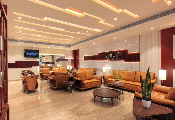 A spacious lobby with leather sofas, a coffee table, and a television mounted on the wall.