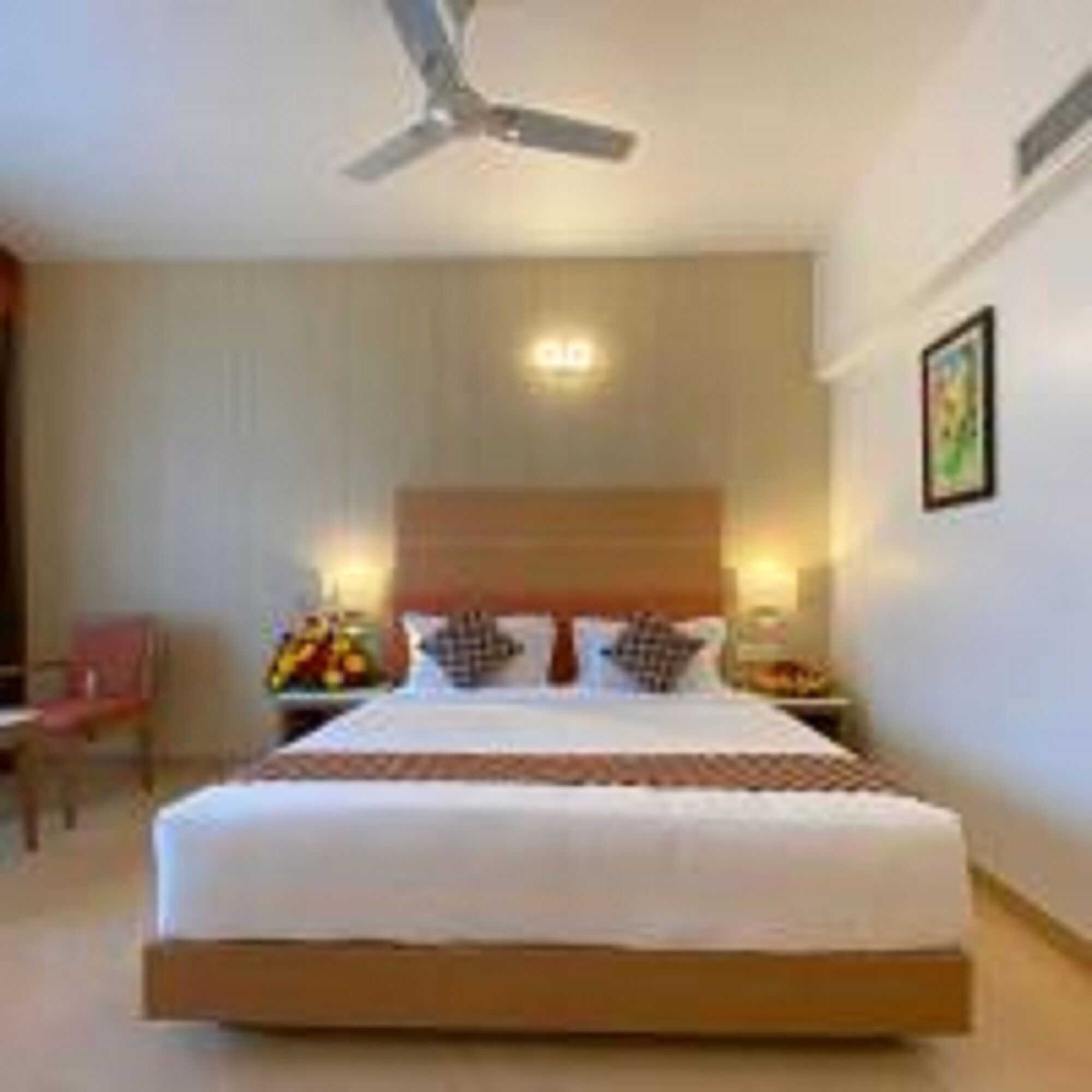 A hotel room with a large bed, a ceiling fan, a nightstand with a lamp, and a chair.