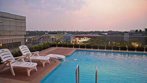 Una piscina en la azotea con sillones de descanso, vistas de la ciudad y, al fondo, un concesionario Jaguar.