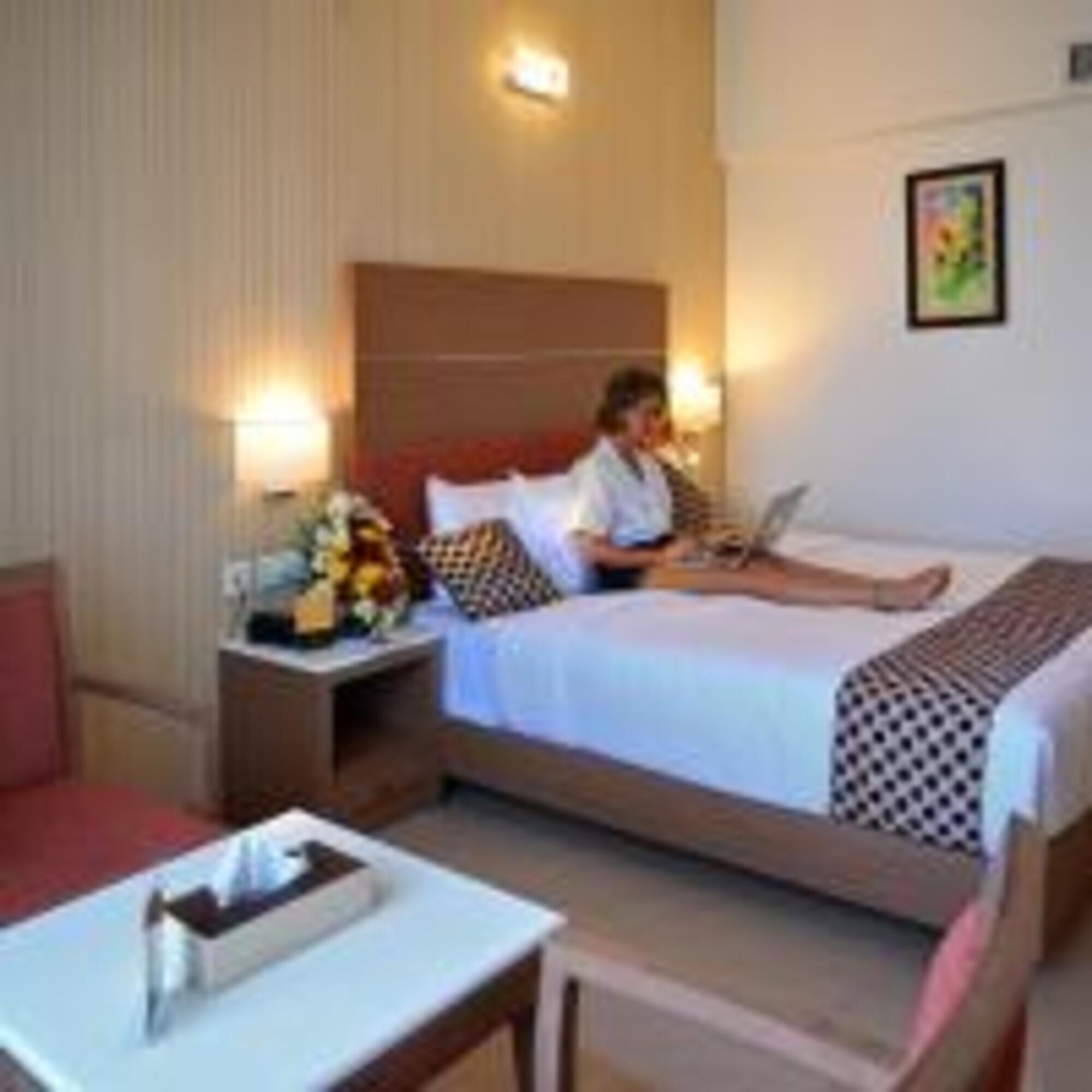 A hotel room with a bed, a desk, a nightstand, and a lamp.
