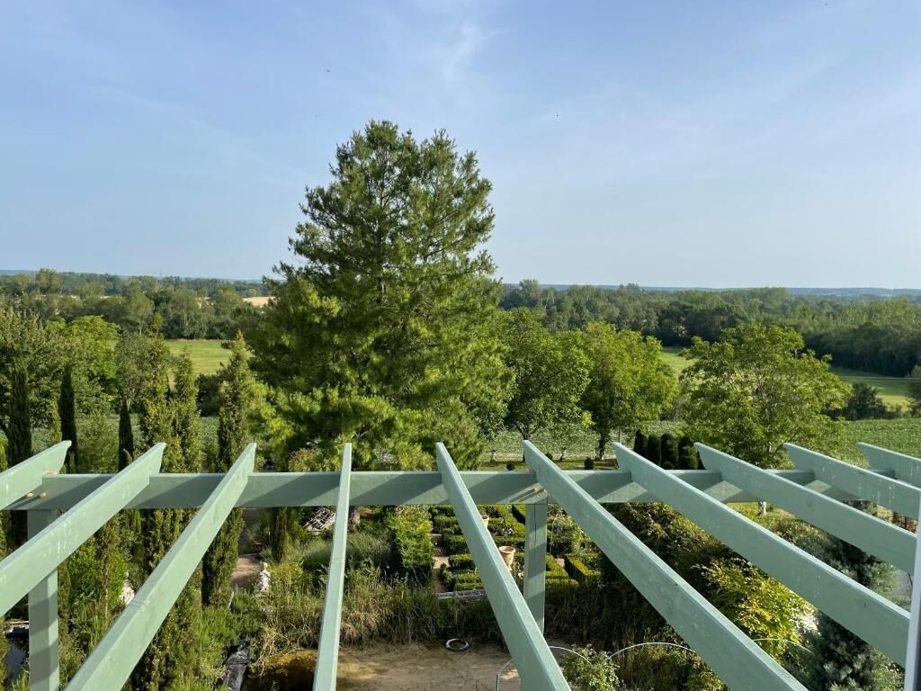 A view from a balcony with a pergola structure, overlooking a landscaped garden with various trees and shrubs.
