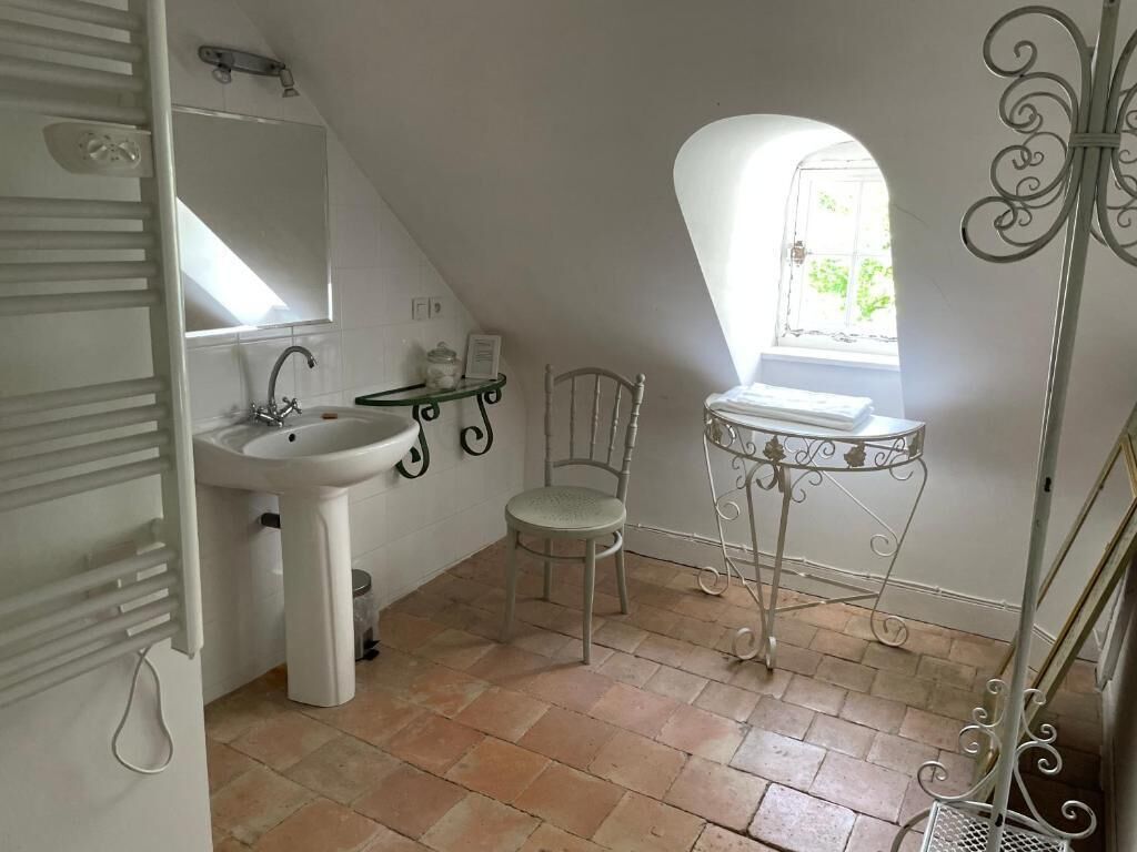 Une petite salle de bain blanche, avec un lavabo, un miroir et une fenêtre.