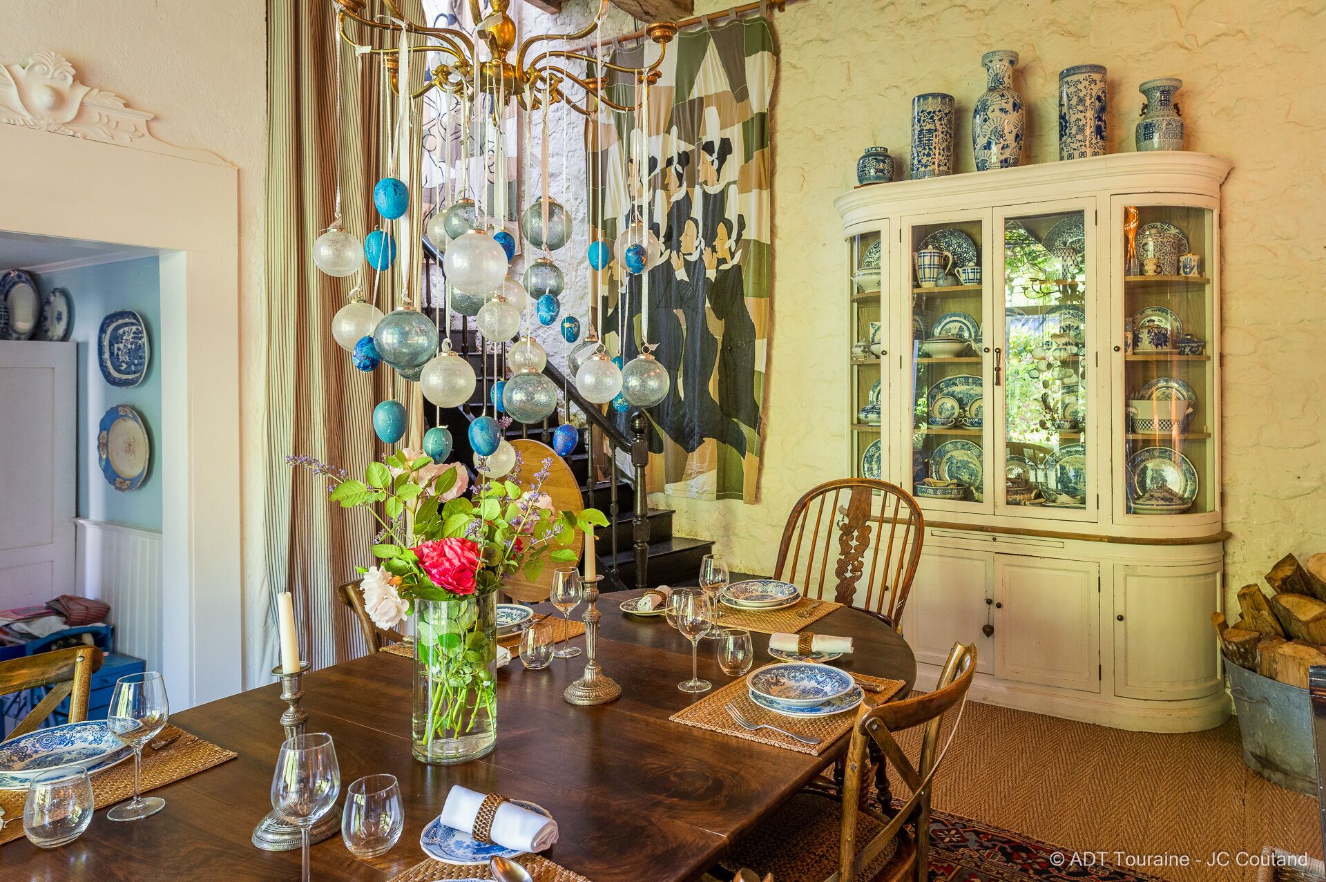 A dining area with a wooden table set for four, a vase with flowers, and a cabinet with glass doors displaying blue and white dishes.