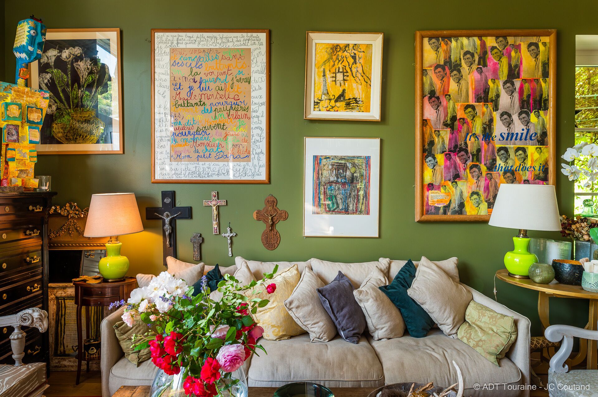 A cozy living room with a sofa, floral arrangement, and various framed artworks on the wall.