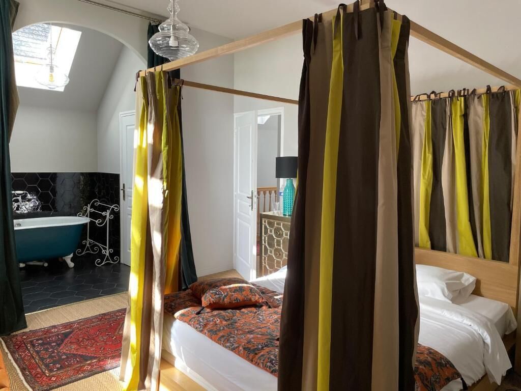 A bedroom with a four-poster bed, a large mirror, and a view of a bathroom with a blue bathtub.