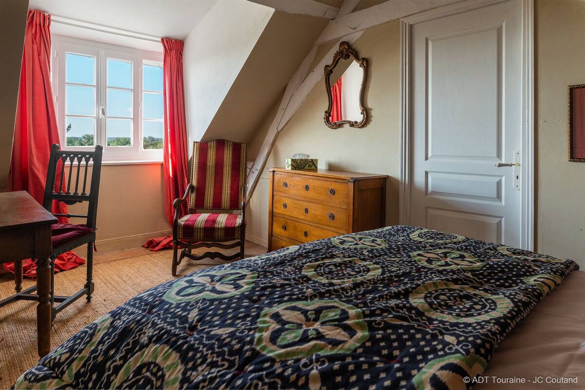 A bedroom with a bed, a chair, a dresser, a mirror, and a window with curtains.