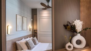 Ein modernes Schlafzimmer mit einem großen Spiegel, einem Bett mit weißen Leinentüchern, einem Deckenventilator und dekorativen Vasen auf einem Holzregal.
