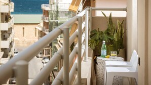Ein Balkon mit Blick auf den Strand, ein Tisch mit Flasche und Glas sowie Kübelpflanzen.