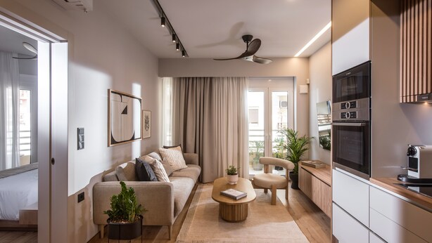 Ein modernes Wohnzimmer mit einer Couch, einem Couchtisch und einem Deckenventilator. Es gibt eine Küchenzeile mit einer Mikrowelle und einem Backofen.