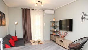 A modern living room with a grey sofa, a wooden coffee table, a TV mounted on the wall, and a black chair. - Ariadni s Athenian Apartment (Athens)