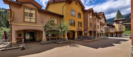 Un patio con zona pavimentada, un edificio de fachada amarilla y una montaña al fondo.