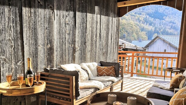 A wooden deck with a sofa, a small table with glasses and a bottle, and candles. - Appartement Chez Léon Avec Jardin (Samoëns)