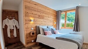A bedroom with a wooden headboard, a bed with white bedding, a nightstand, and a window with curtains. - Appartement Chez Léon Avec Jardin (Samoëns)