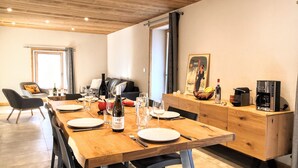 A dining area with a wooden table set for four, a coffee machine, and a painting on the wall. - Appartement Chez Léon Avec Jardin (Samoëns)