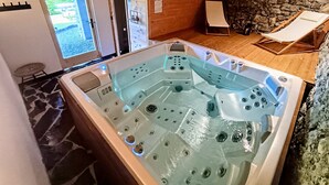 A hot tub with jets, a stone floor, a wooden ceiling, and a stone wall. - Appartement Chez Léon Avec Jardin (Samoëns)